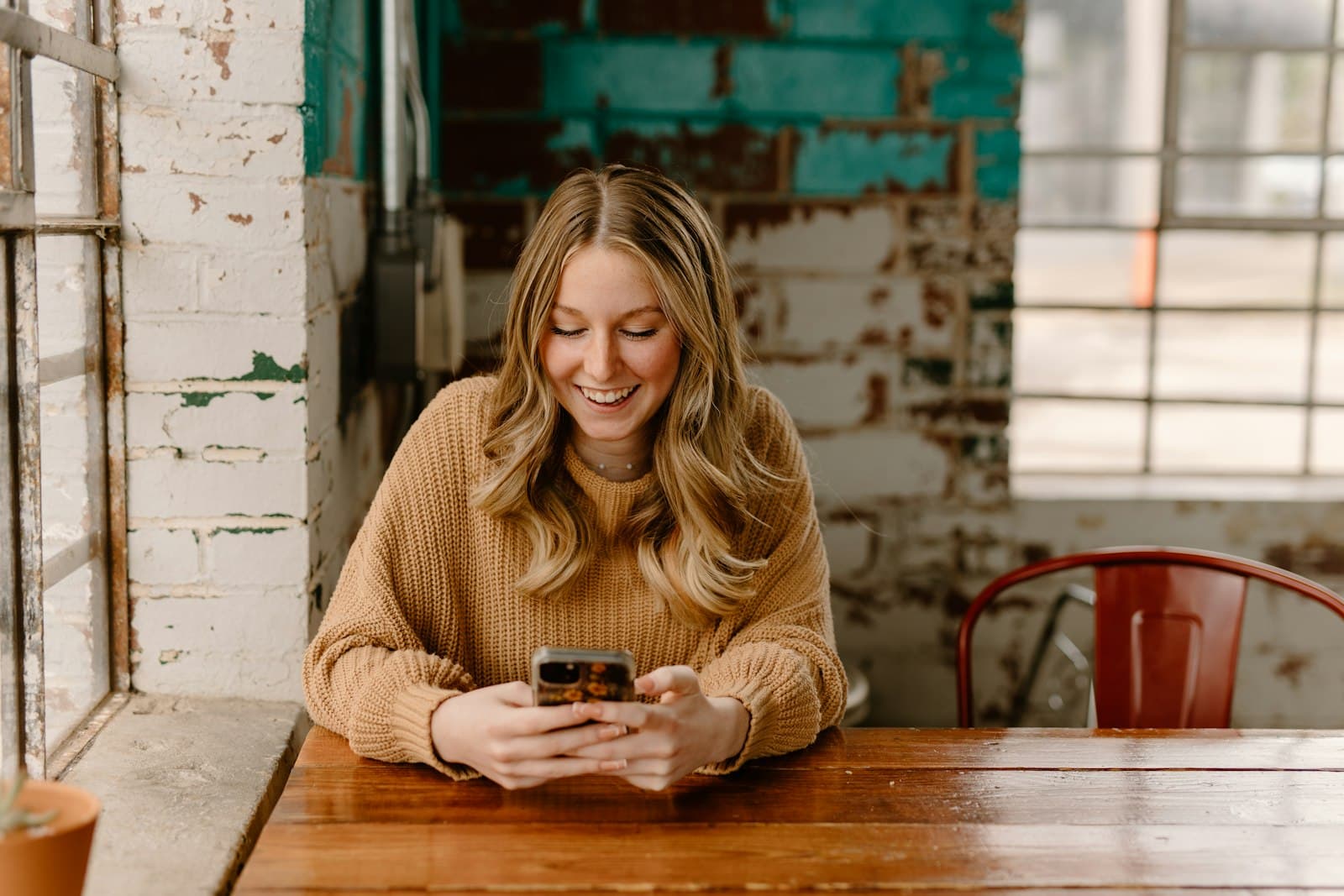 A woman smiling at her phone at a café table
