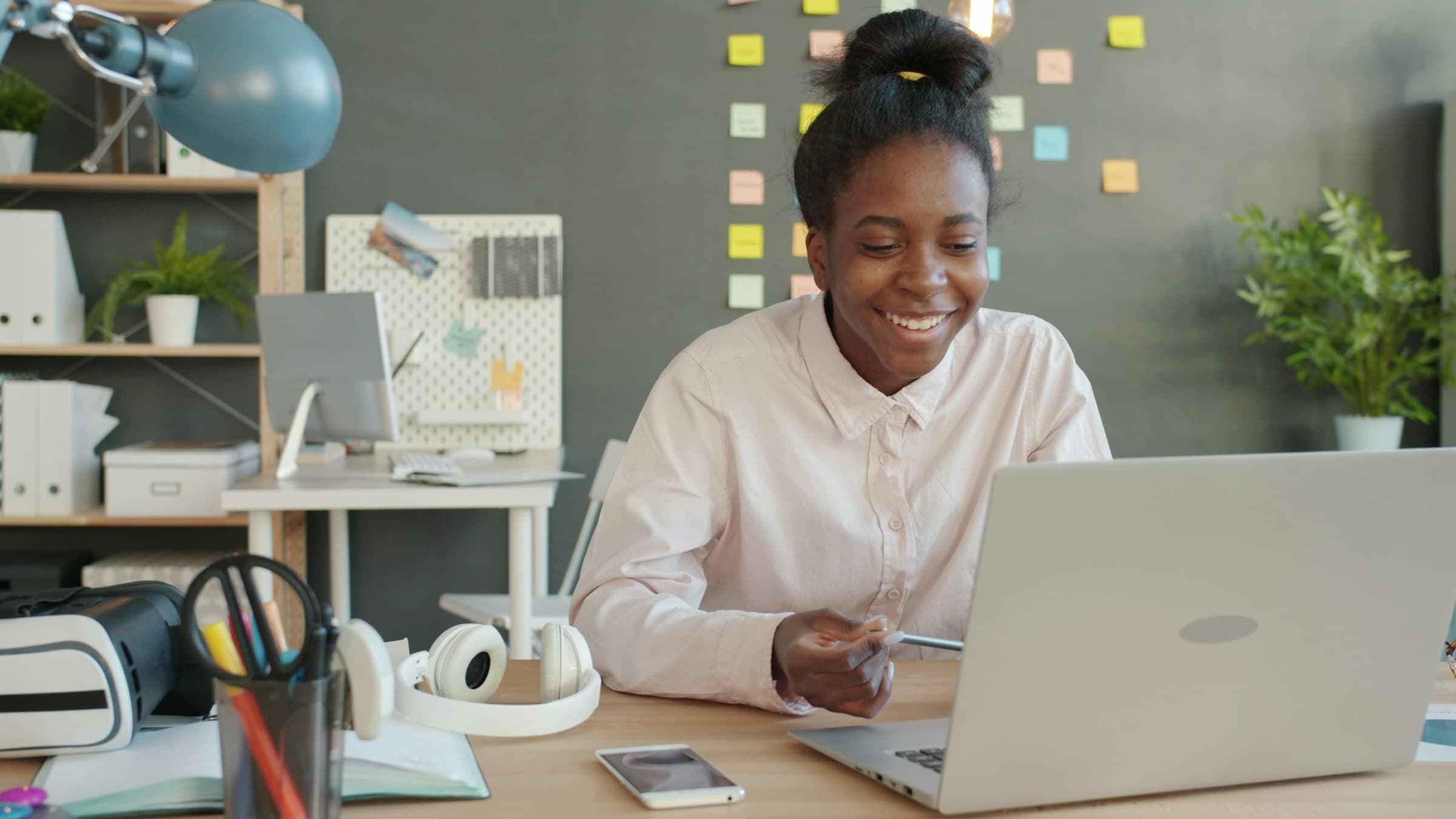 A freelancer smiling at her laptop in a bright studio with a pinboard behind her